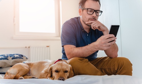 Homem ao celular com um cachorro deitado ao lado